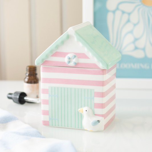 Pastel striped beach hut with a small bird decoration on a white surface.