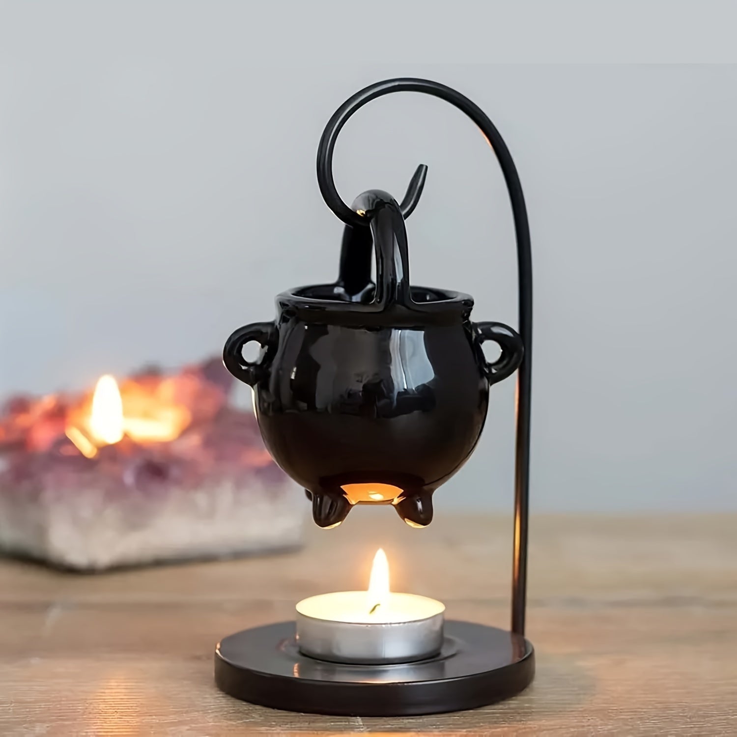 Black cauldron-shaped candle holder with a lit candle on a wooden surface.