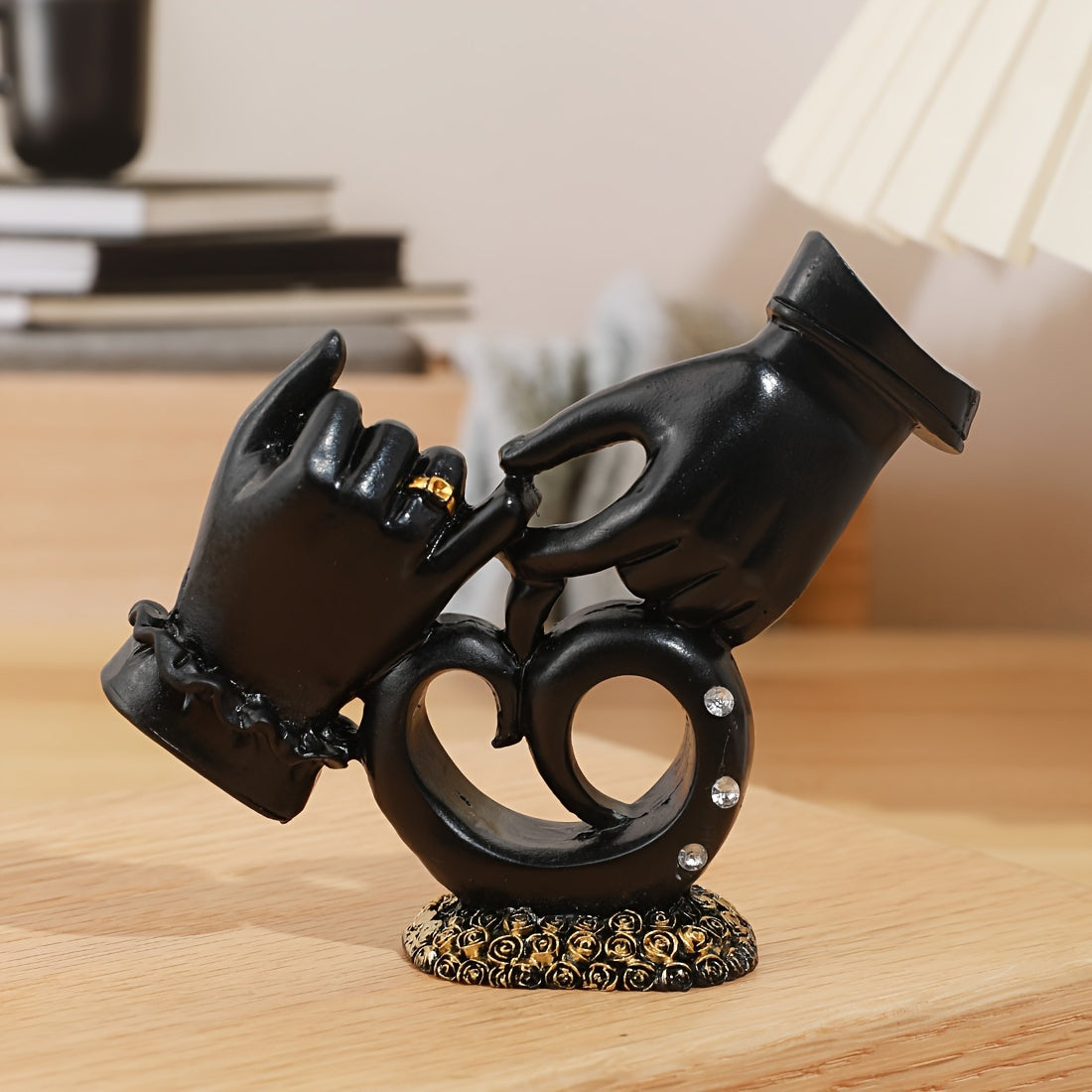 Decorative black sculpture of hands holding a ring on a wooden surface