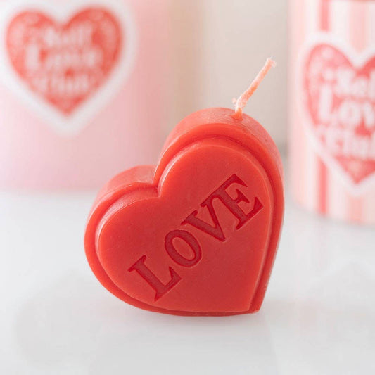 Heart-shaped candle with 'LOVE' embossed on it, set against a blurred background with heart designs.