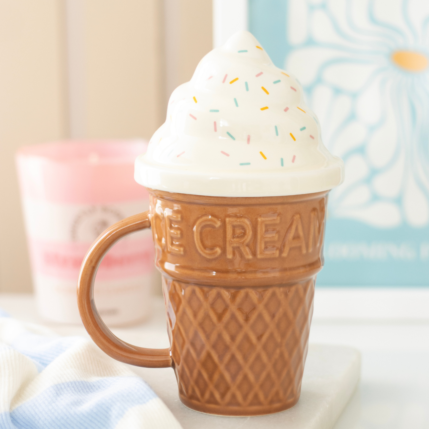 Ice cream cone mug with whipped cream and sprinkles on a soft surface.