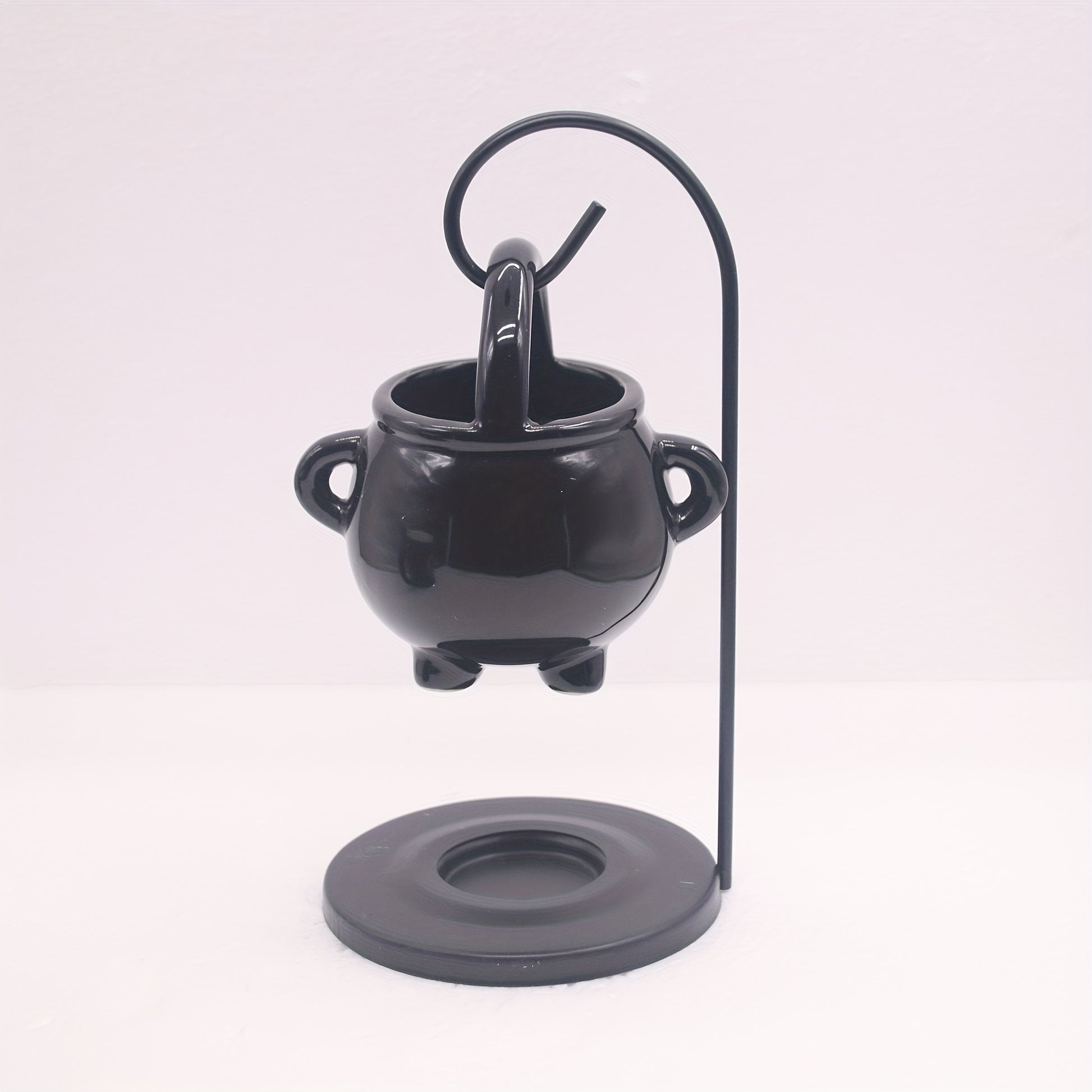 Black cauldron-shaped holder with a candle on a white background