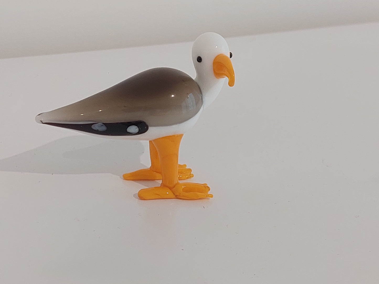 Toy bird figurine with a white head, gray body, and orange feet on a white background